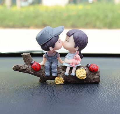 Car dashboard couple figurines kissing with blue cap, ladybug accents, and bear