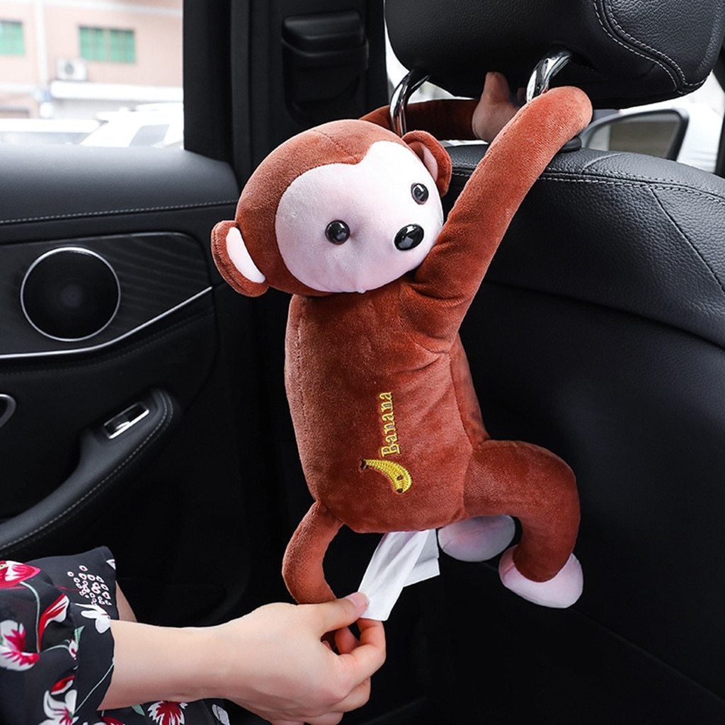 Brown plush monkey tissue holder, hanging with tissues peeking out in car interior
