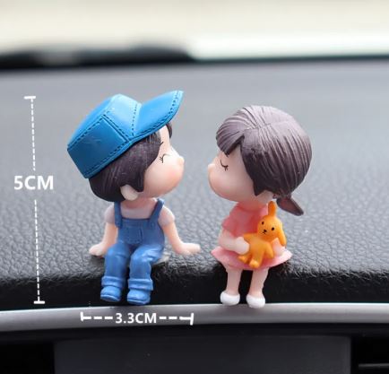 Close-up of kissing car couple figurines with blue cap and orange teddy