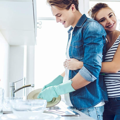 Person wearing blue dishwashing gloves while cleaning dishes at the kitchen sink