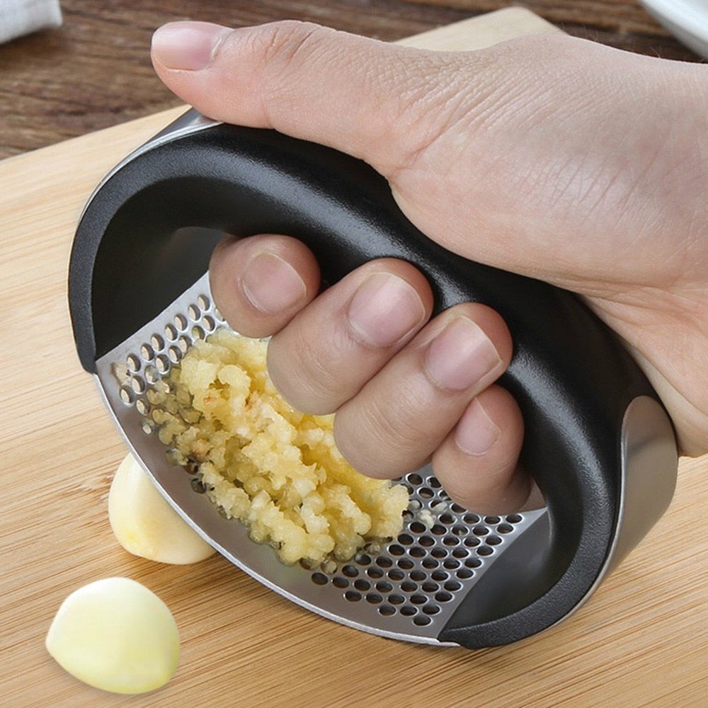 Garlic press held in hand, crushing garlic into a minced pile