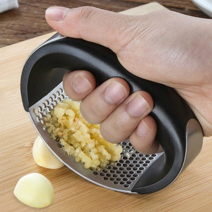 Garlic press held in hand, crushing garlic into a minced pile
