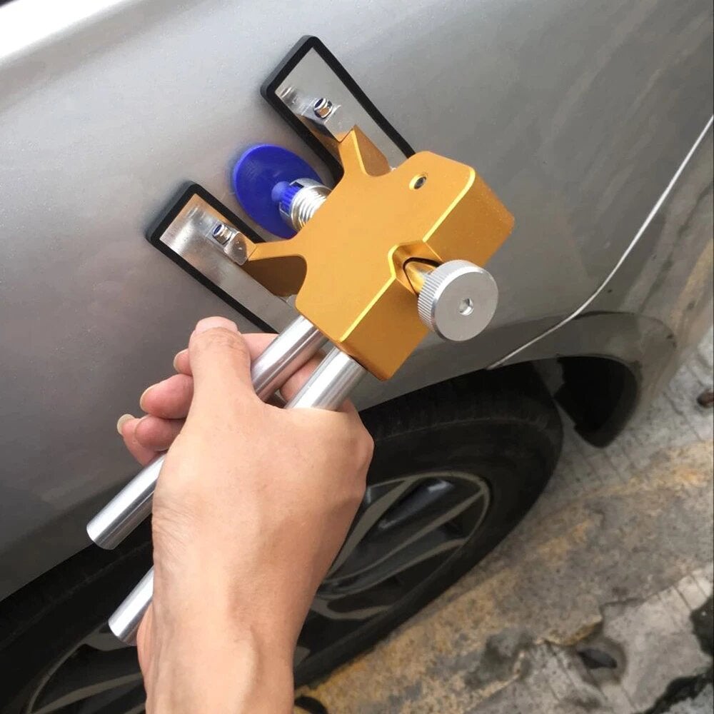 Hand using gold dent puller tool with two rods on a car panel