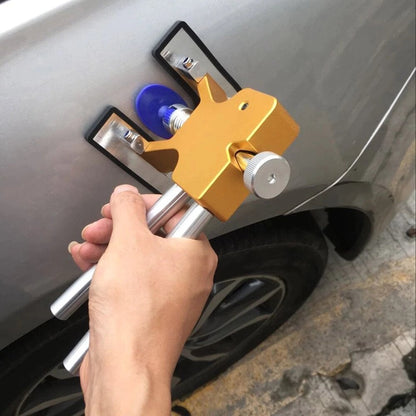 Hand using gold dent puller tool with two rods on a car panel