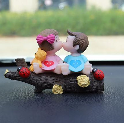 Kissing couple car figurines on dark wood base with pink heart bow and ladybugs