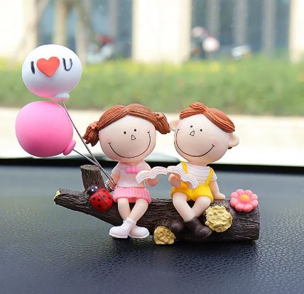 Car dashboard couple figurines with heart balloon and smiling faces on dark wood
