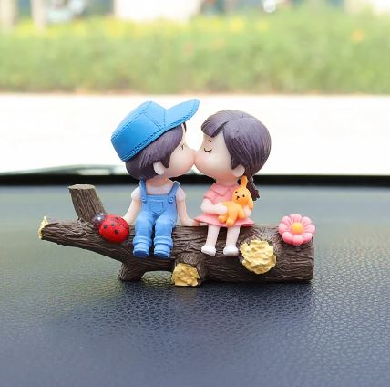 Car dashboard couple figurines kissing with pink balloon and orange teddy