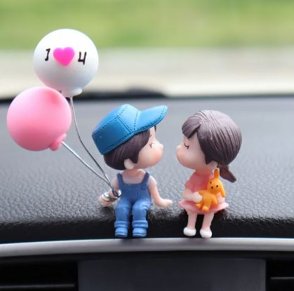 Car dashboard couple figurines kissing with pink heart balloon and blue cap