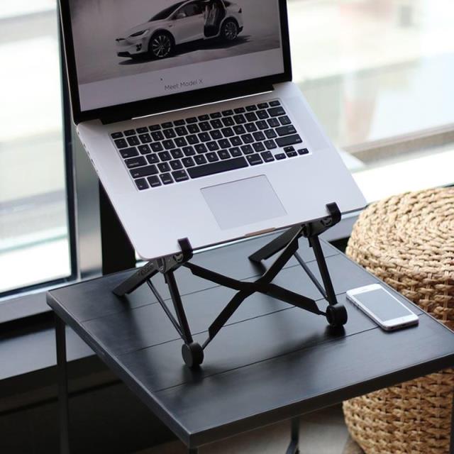 Black adjustable laptop stand holding a laptop on a desk surface