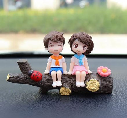 Car dashboard couple figurines sitting on dark wood base with flower and ladybug