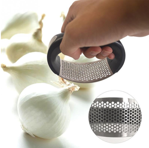 Black garlic press with perforated basket and garlic bulbs nearby